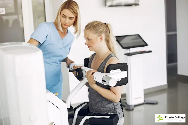 A female physiotherapist instructs a female patient on how to use a gym machine.