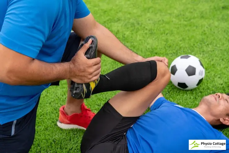 A physiotherapist is gently stretching the raised leg of a male soccer player.