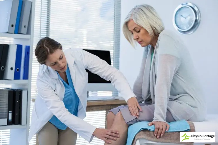 A physiotherapist leans over examine the knee of an older female patient.