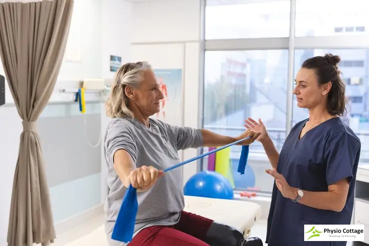 A female physiotherapist assists an older woman in-clinic exercise.