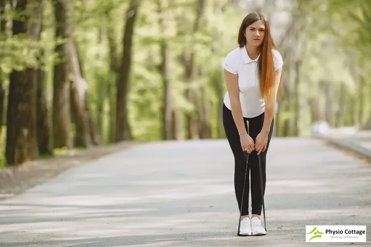 Woman in a white shirt bending over, holding a resistance band for exercise.
